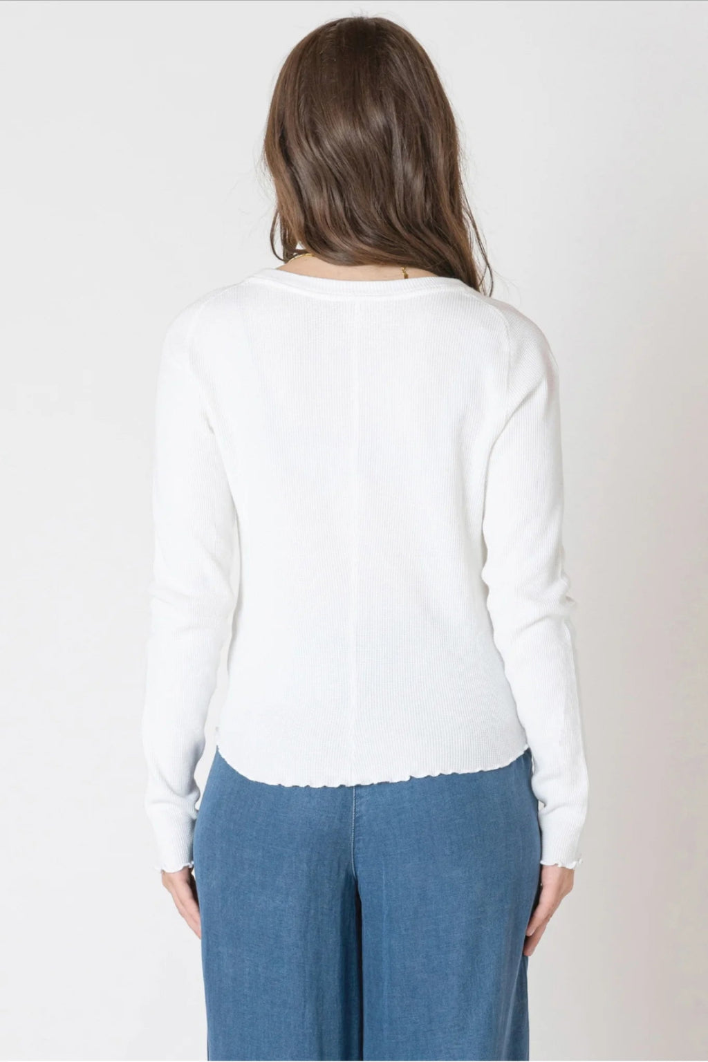 Person wearing a white sweater and blue pants on a plain background.