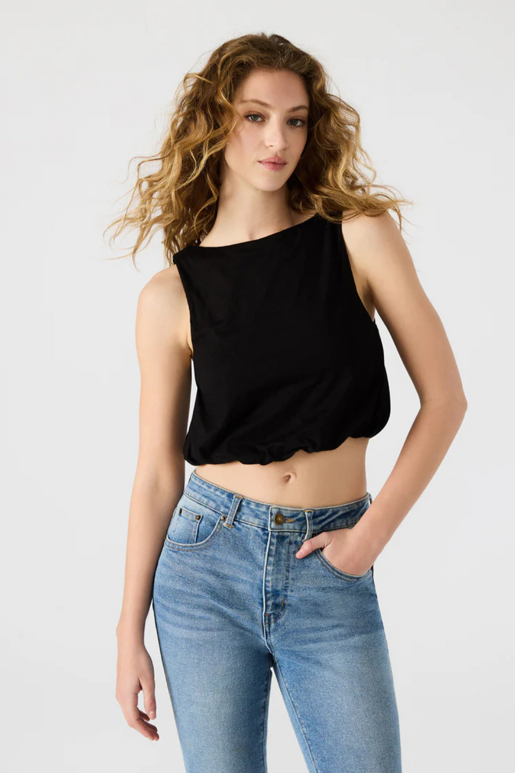 A woman wearing a black crop tank with denim jeans. 