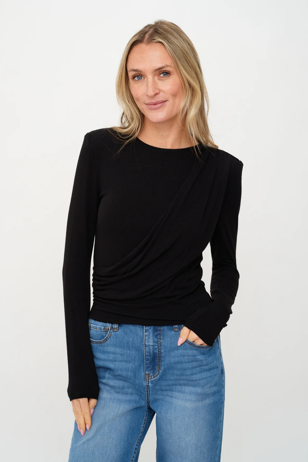 Woman wearing a black long-sleeve top and blue jeans on a white background.