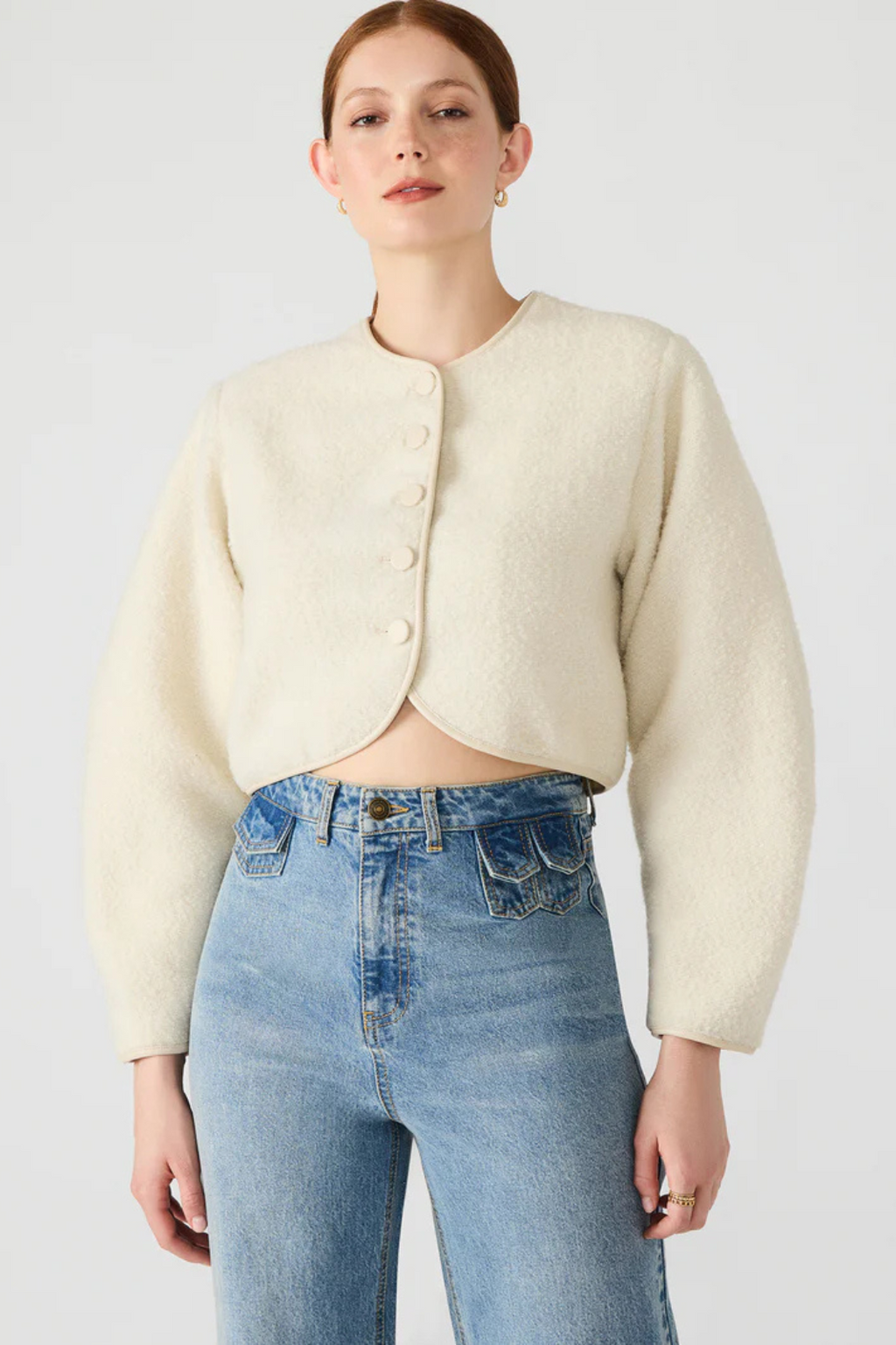 Woman wearing a cream jacket and blue jeans on a white background.