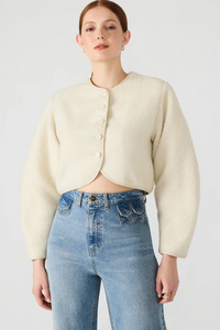 Woman wearing a cream jacket and blue jeans on a white background.
