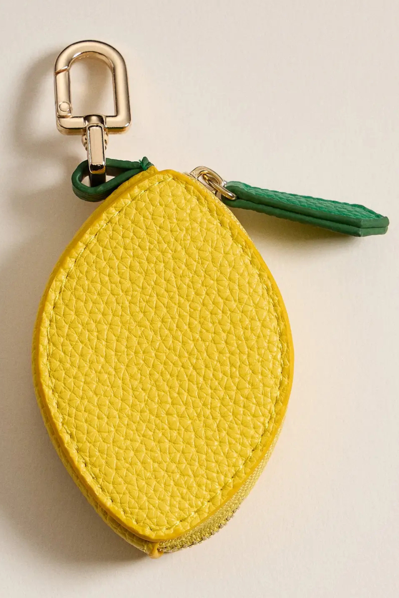 Yellow lemon-shaped keychain with a gold clip on a beige background.