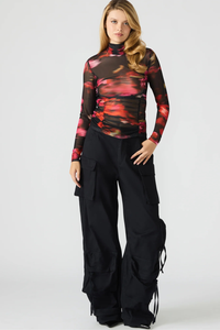 Woman wearing a colorful top and black pants on a white background.