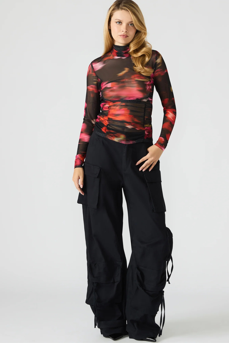 Woman wearing a colorful top and black pants on a white background.