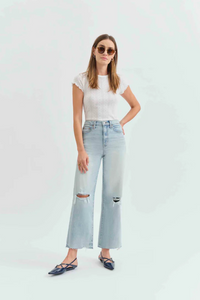 Front view of a woman wearing a white t-shirt with light denim jeans with holes in the knees, and pointed flats. 