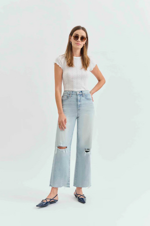 Front view of a woman wearing a white t-shirt with light denim jeans with holes in the knees, and pointed flats. 