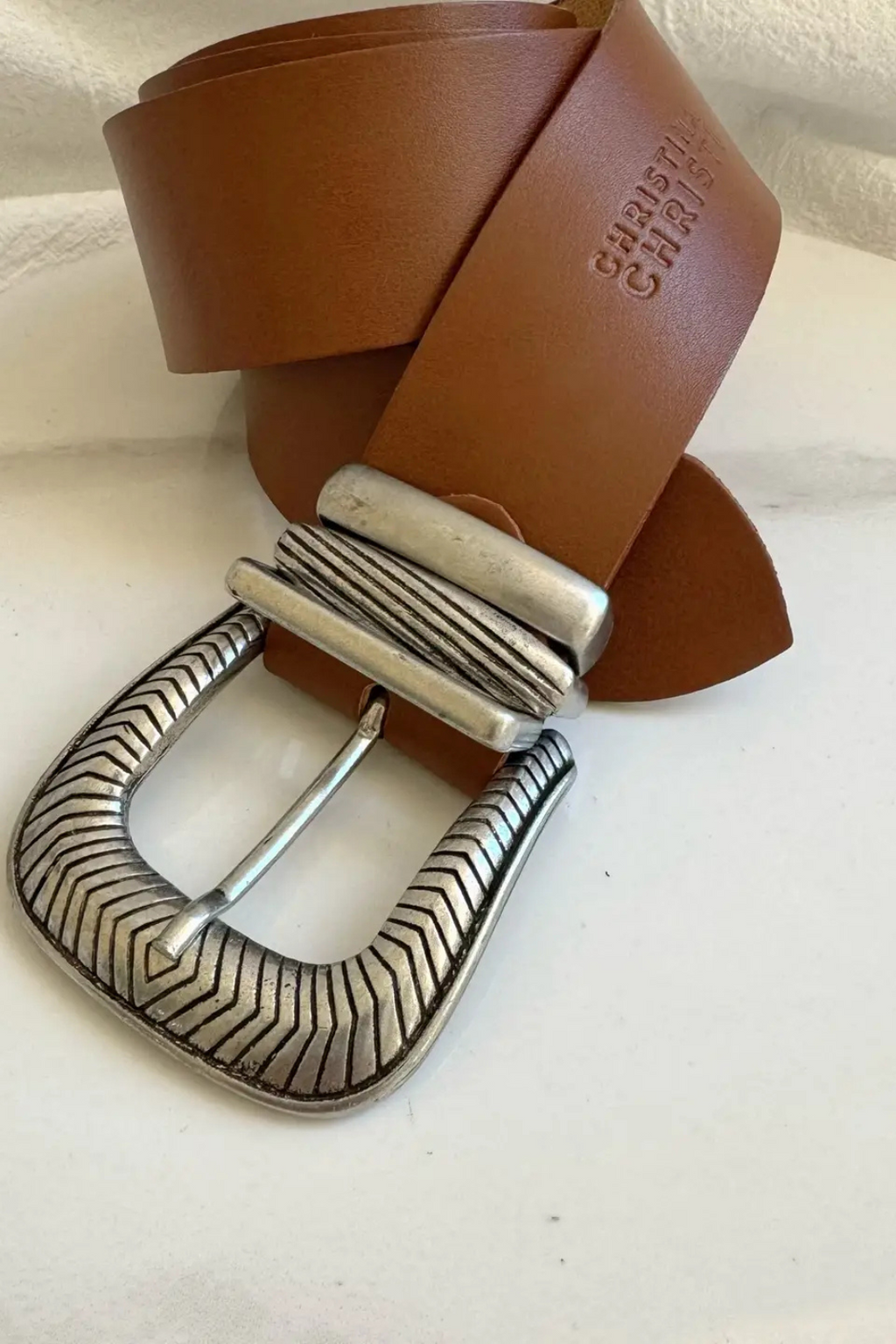 A close up shot of a taupe belt with silver buckles.