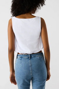 A back view of a woman wearing a white cropped tank top and denim jeans. 