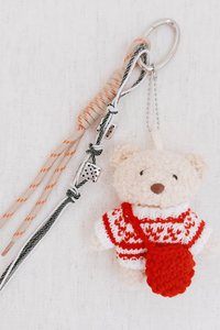 Knitted bear keychain with a red scarf on a light background.