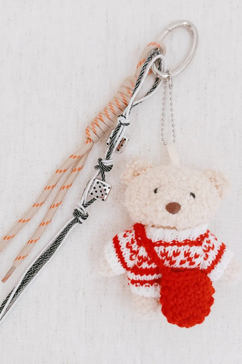 Knitted bear keychain with a red scarf on a light background.