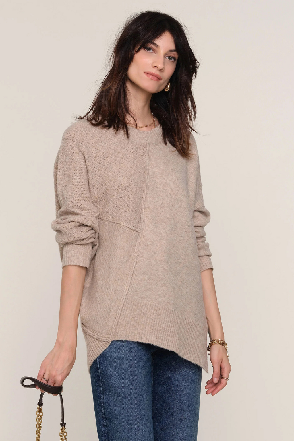 Woman wearing a beige sweater and blue jeans against a plain background.