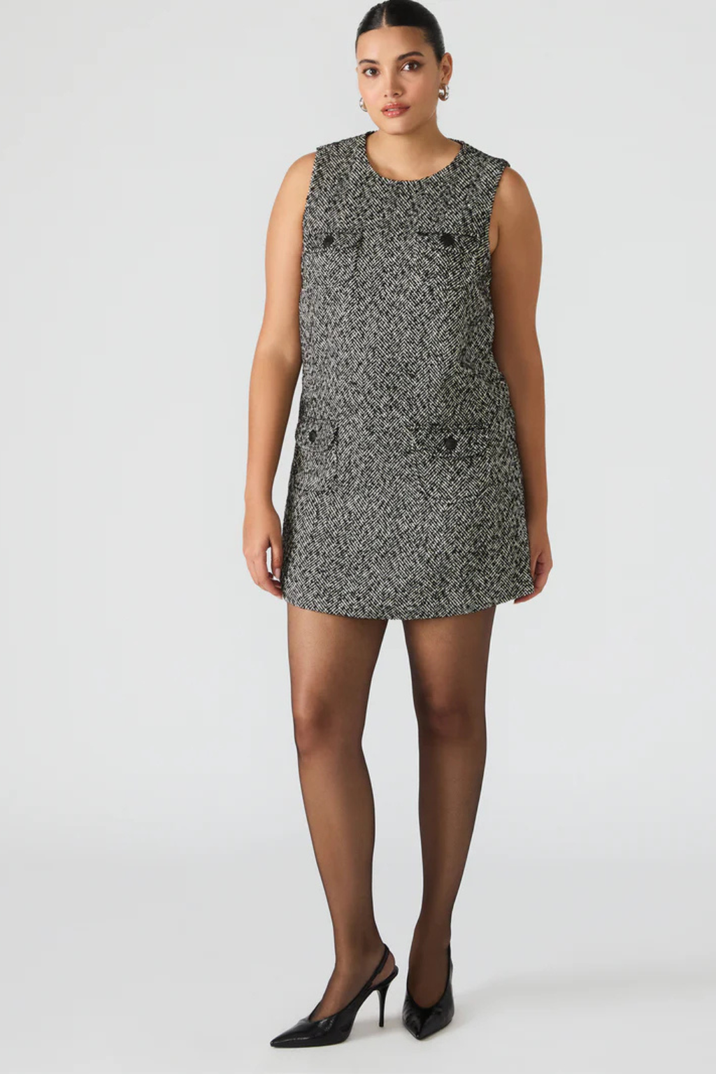 A woman wearing a patterened mini dress with black heels. 