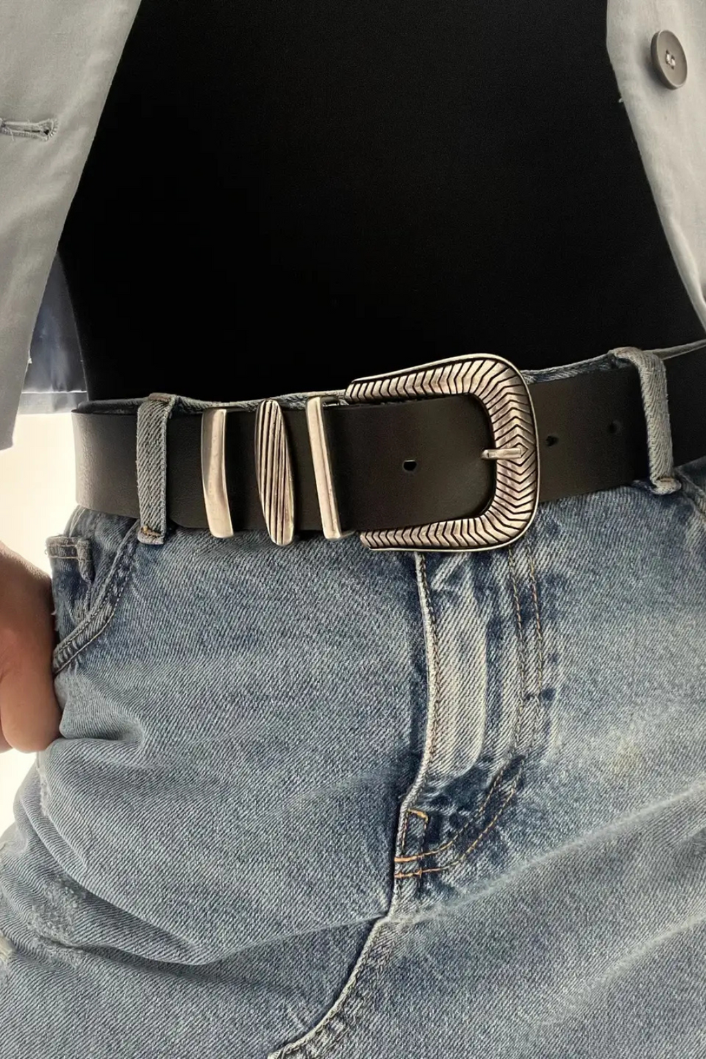 Woman wearing a black shirt, a denim skirt with a black and silver buckle belt.