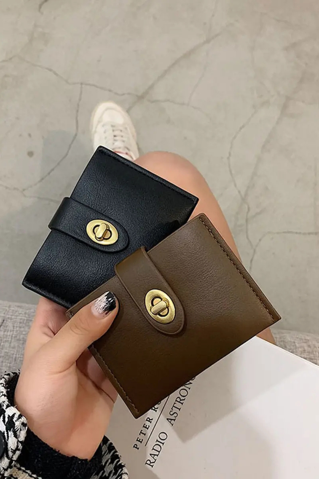 Two wallets, one black and one brown, held by a hand on a textured surface.