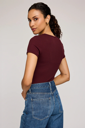 Woman wearing a burgundy top and blue jeans against a plain background.