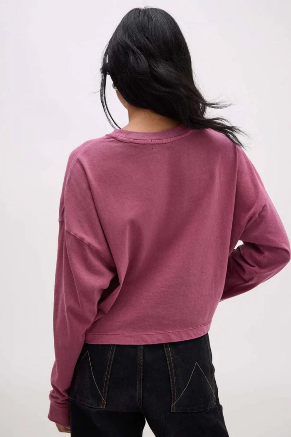 Back view of a woman wearing a long sleeve mauve shirt and dark denim.