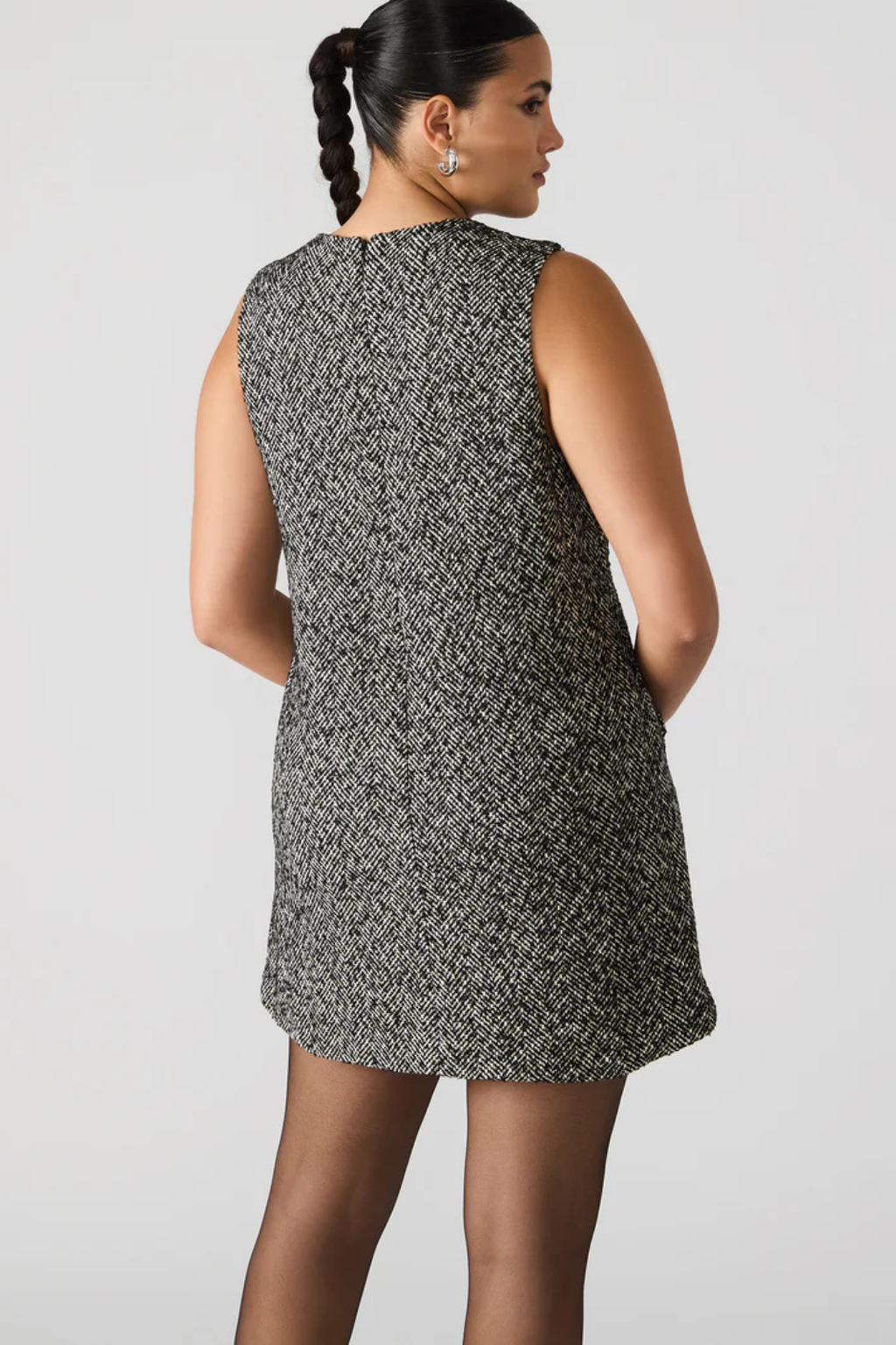 Woman wearing a sleeveless patterned dress against a plain background.