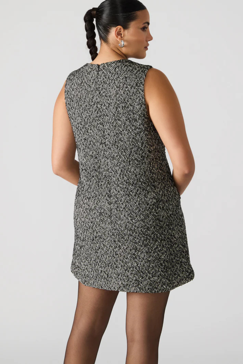 Woman wearing a sleeveless patterned dress against a plain background.