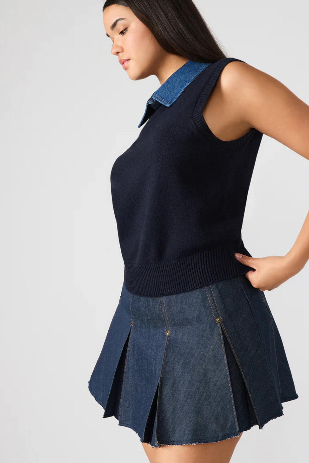 Woman wearing a black sleeveless sweater with a denim collar and matching skirt on a white background.