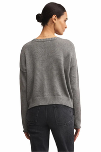 Woman wearing a gray sweater and dark jeans on a white background.
