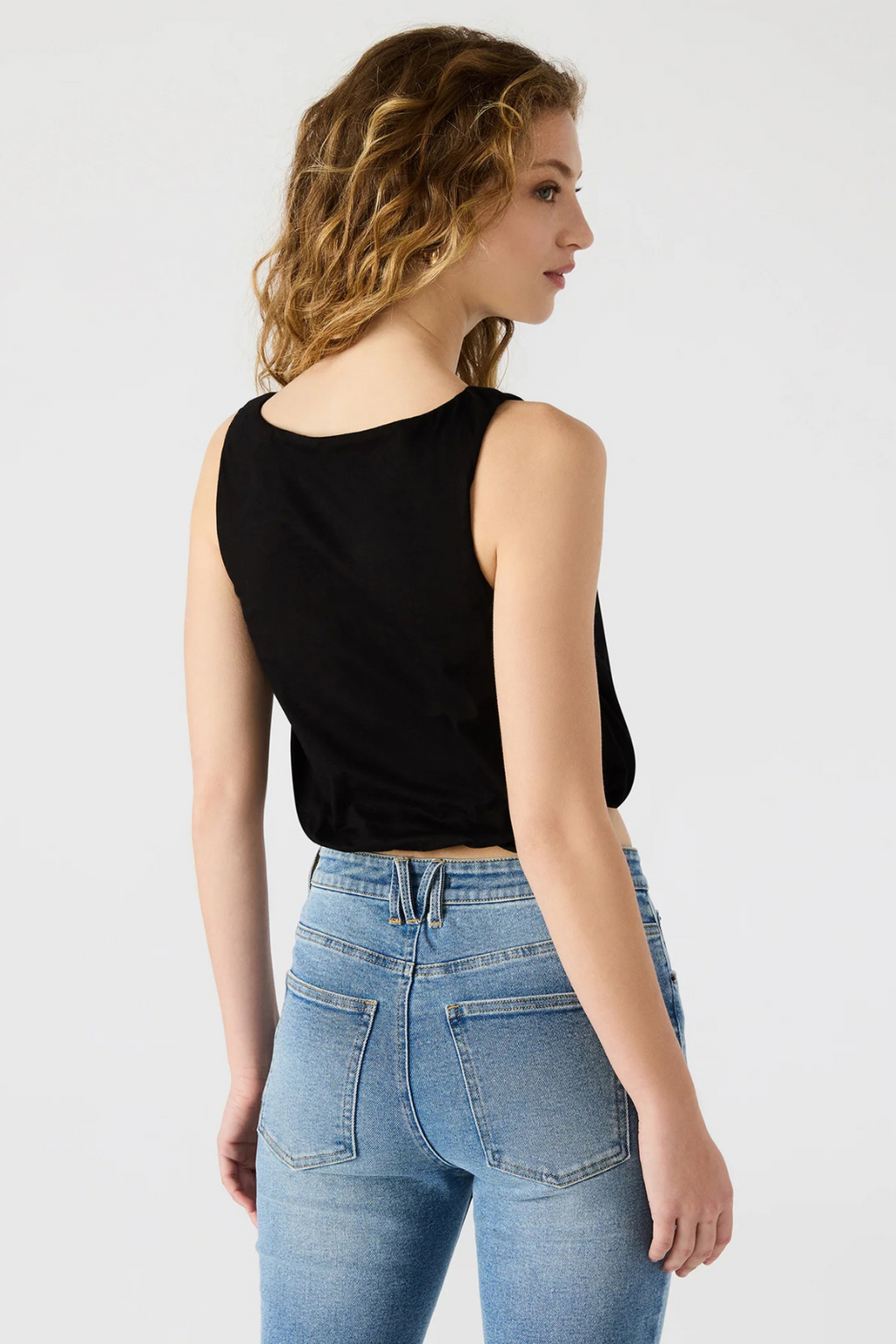 A back side view of a woman wearing a black crop tank and denim jeans. 