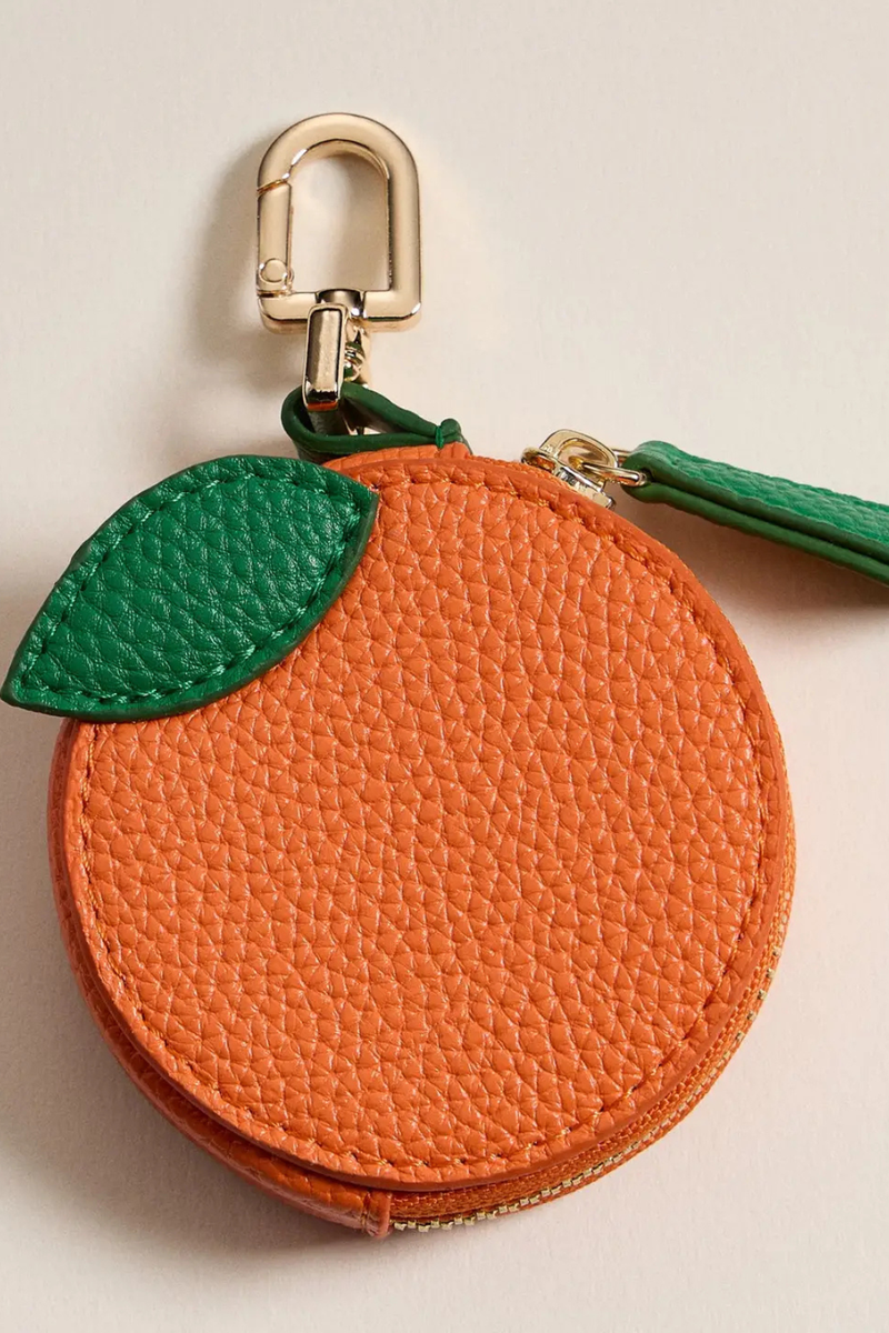 Orange keychain with a green leaf on a beige background.