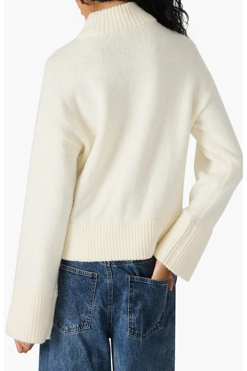 Person wearing a cream sweater and blue jeans on a white background.