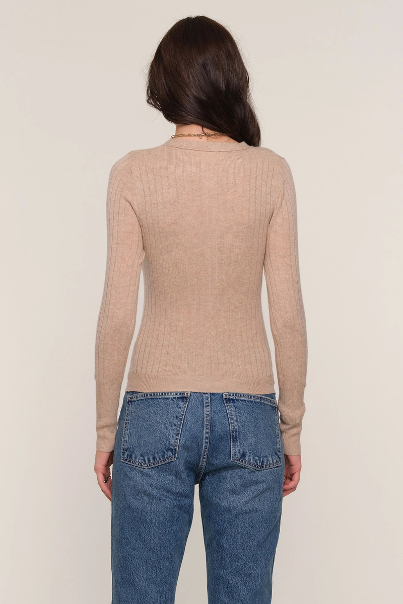 Person wearing a beige ribbed sweater and blue jeans against a plain background.