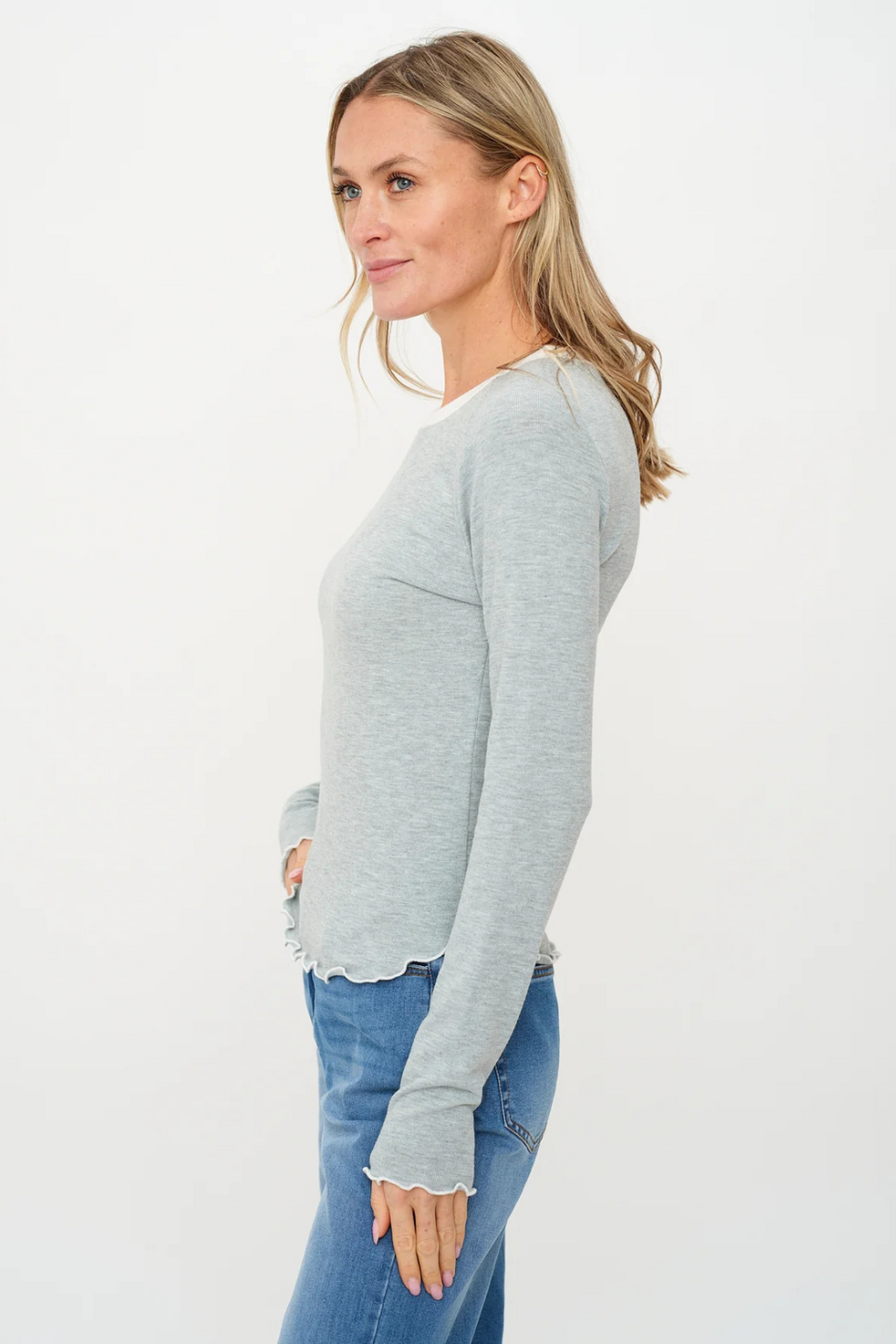 Woman wearing a light gray sweater and blue jeans on a white background.