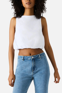 A woman wearing a white cropped tank top with denim jeans. 