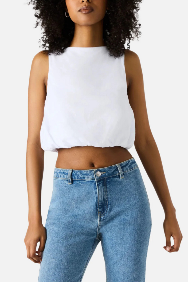 A woman wearing a white cropped tank top with denim jeans. 