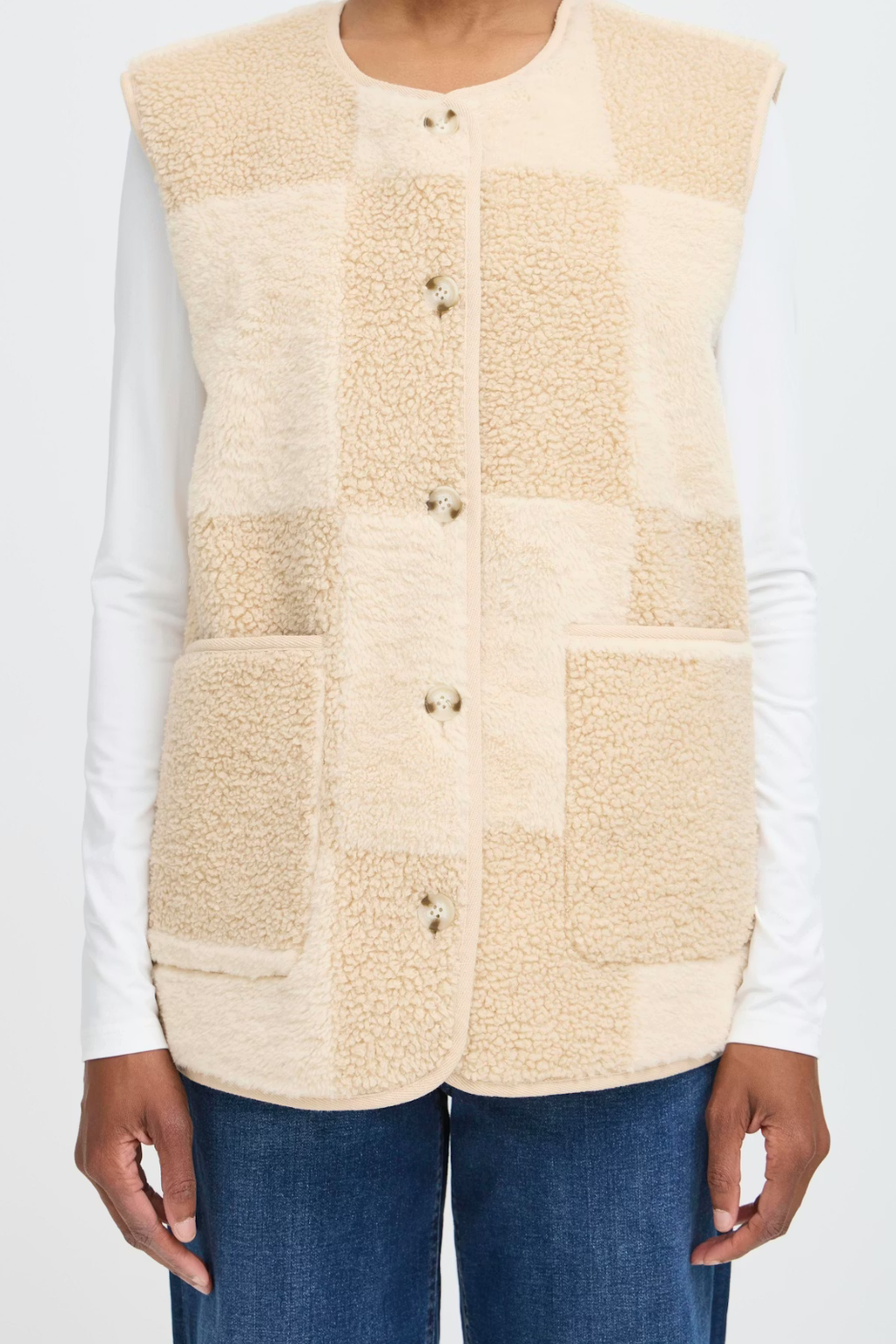 Beige patchwork vest worn over a white shirt and blue jeans on a light gray background.