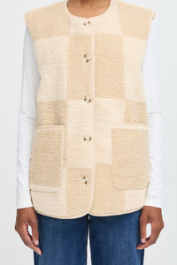 Beige patchwork vest worn over a white shirt and blue jeans on a light gray background.