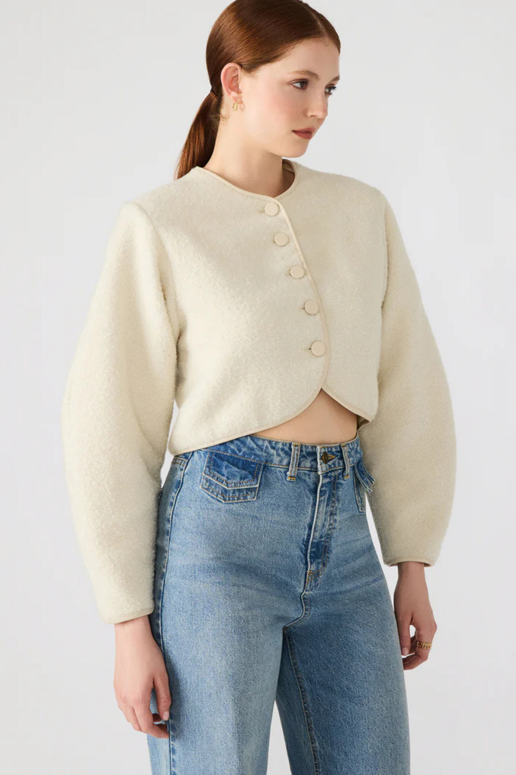 Woman wearing a cream jacket and blue jeans on a white background.