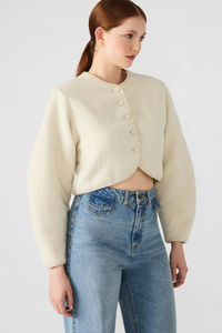 Woman wearing a cream jacket and blue jeans on a white background.