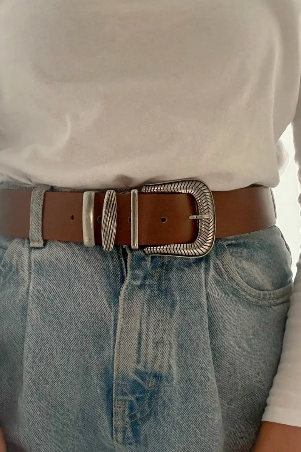 A woman wearing a white shirt and a denim skirt with a taupe belt and silver buckle.