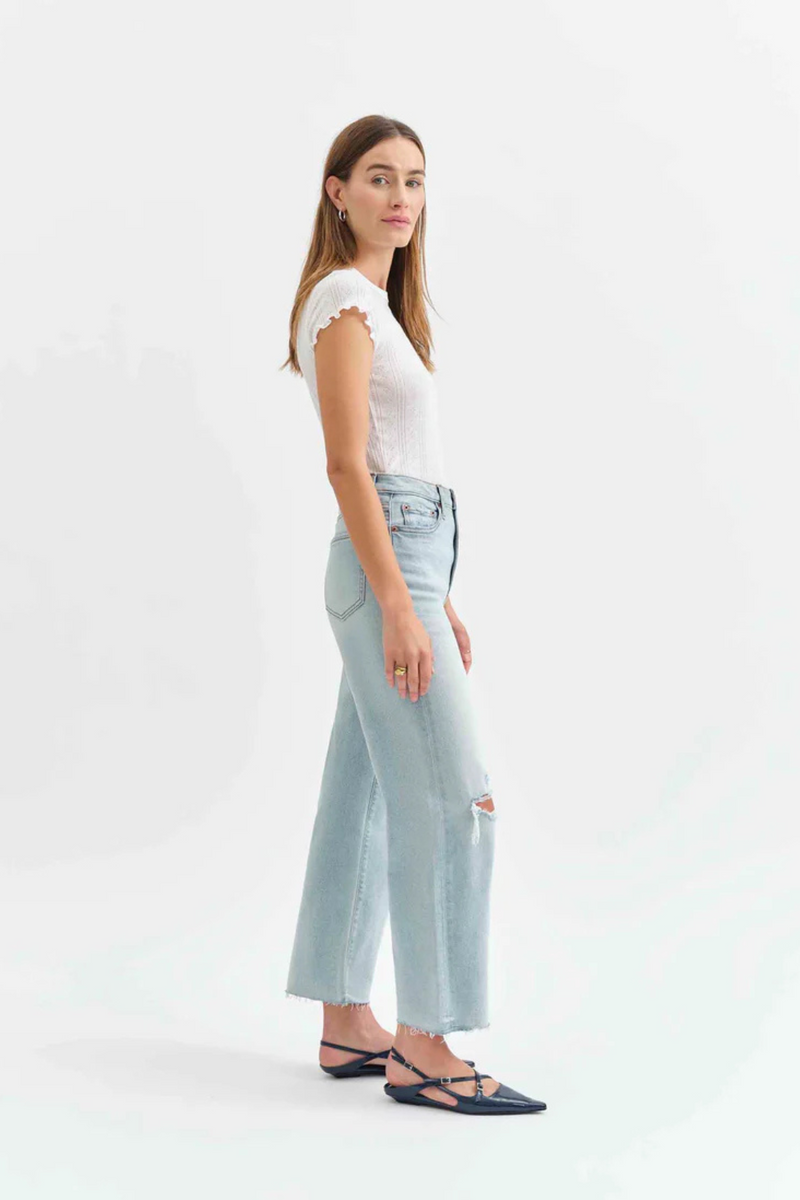 Side view of a woman wearing a white t-shirt with light denim jeans with holes in the knees, and pointed flats. 