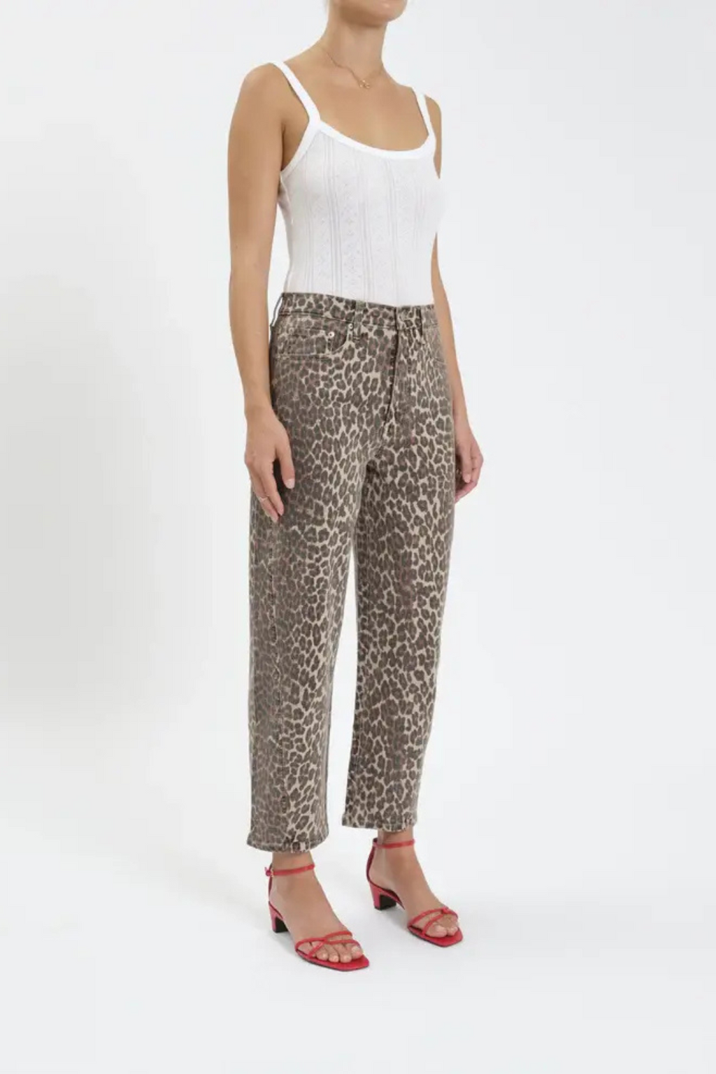 A side view of a woman wearing a white tank top and leopard barrel jeans, with red heels 