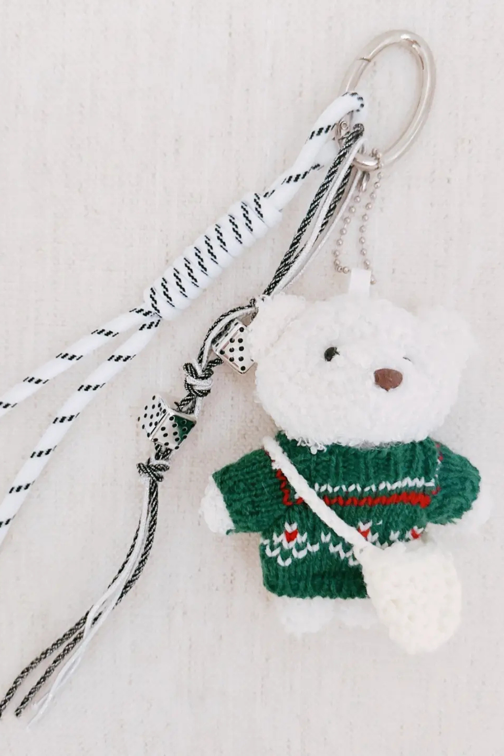 Keychain with a white bear wearing a green sweater on a light background.