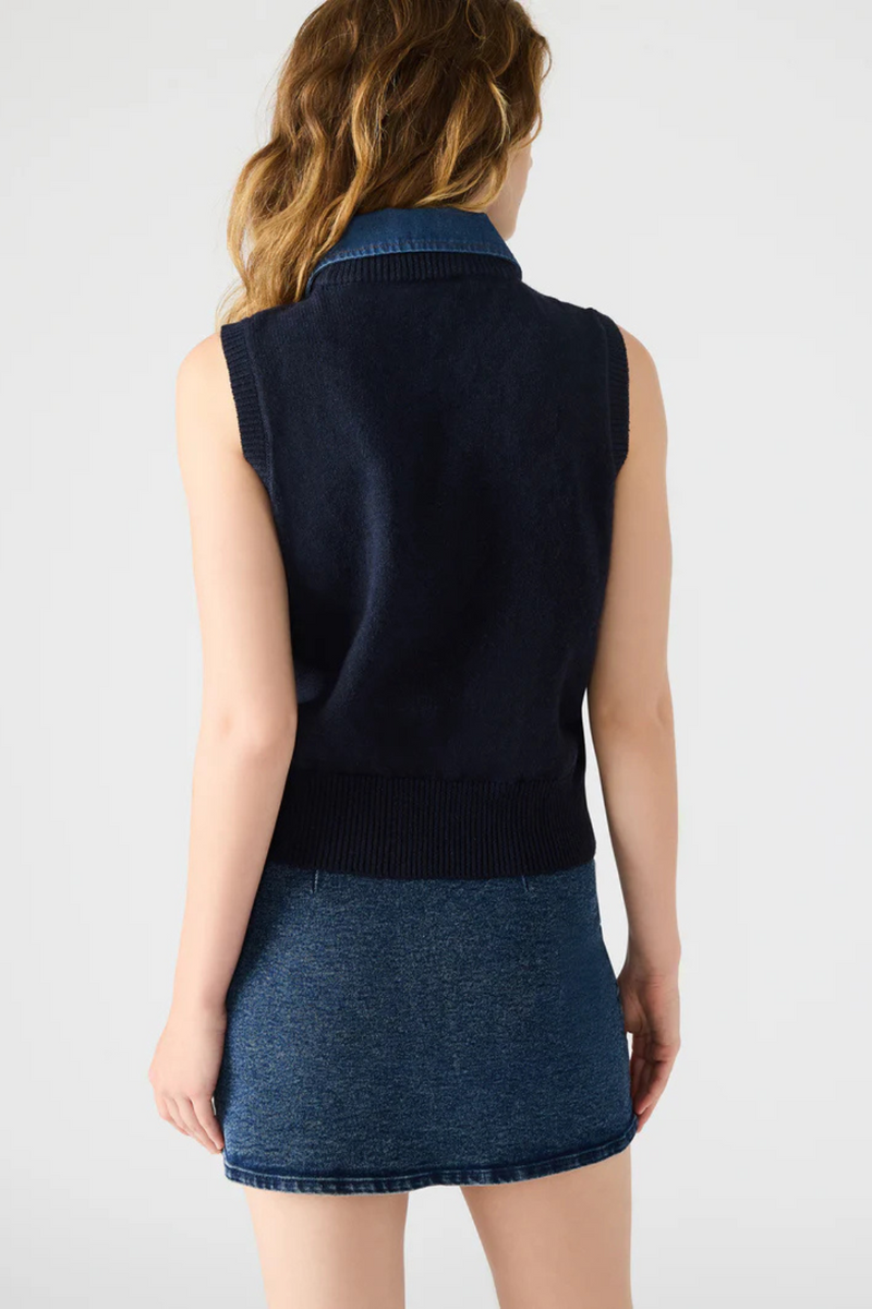 Woman wearing a navy blue sleeveless top and denim skirt on a white background.