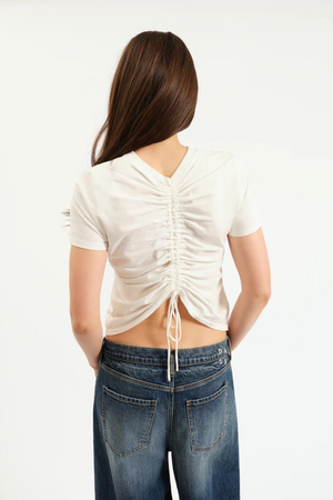 Person wearing a white ruched top and blue jeans on a white background.