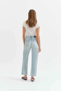 Back view of a woman wearing a white t-shirt with light denim jeans with holes in the knees, and pointed flats. 