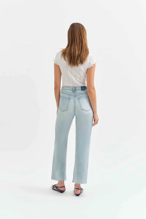 Back view of a woman wearing a white t-shirt with light denim jeans with holes in the knees, and pointed flats. 