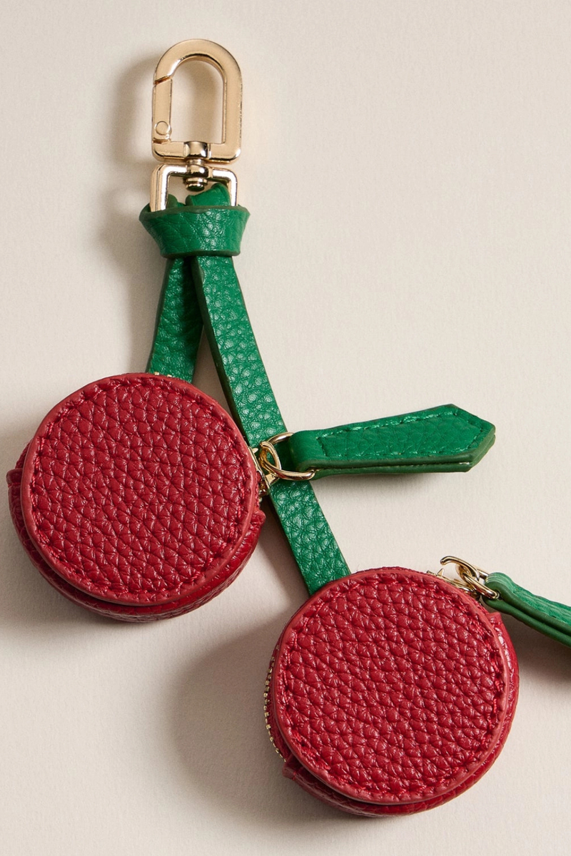Red cherry keychain with green straps on a beige background.