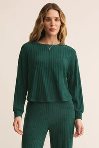 Woman wearing a green ribbed sweater and pants on a beige background.