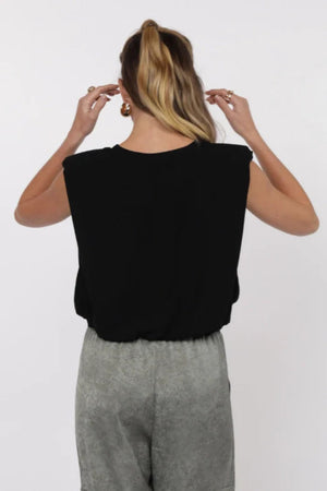 Person wearing a black sleeveless top and gray pants on a white background.