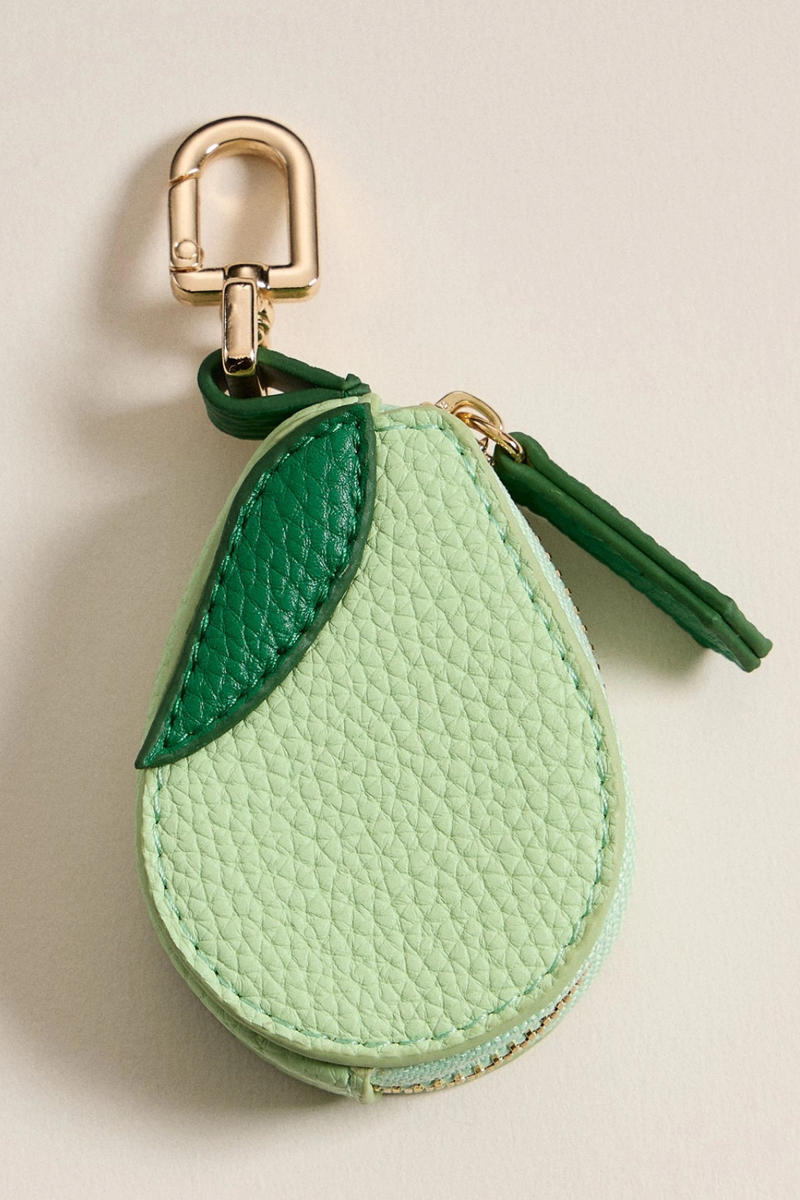 Green avocado-shaped keychain with a gold clip on a beige background.