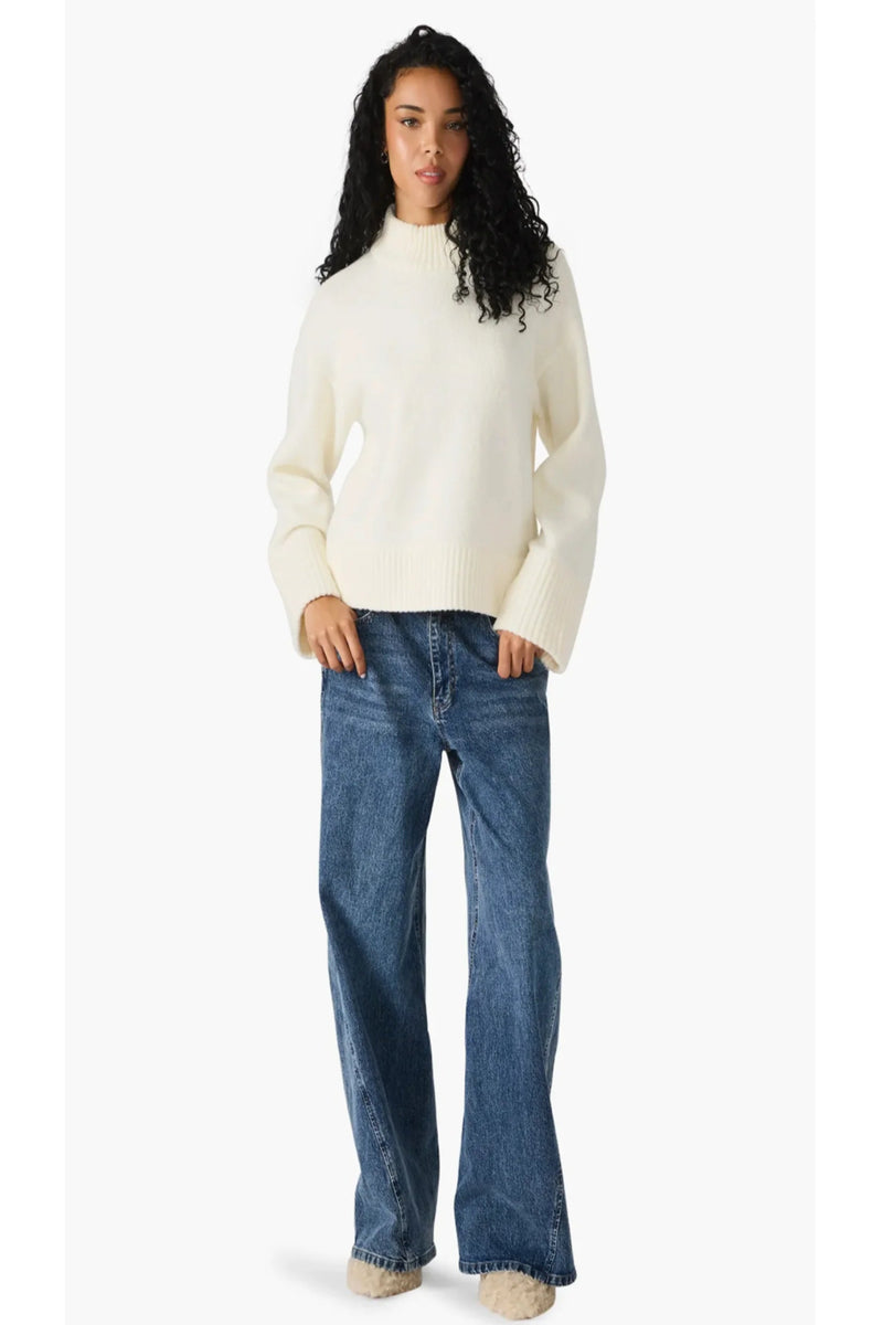 Woman wearing a cream sweater and blue jeans on a white background.
