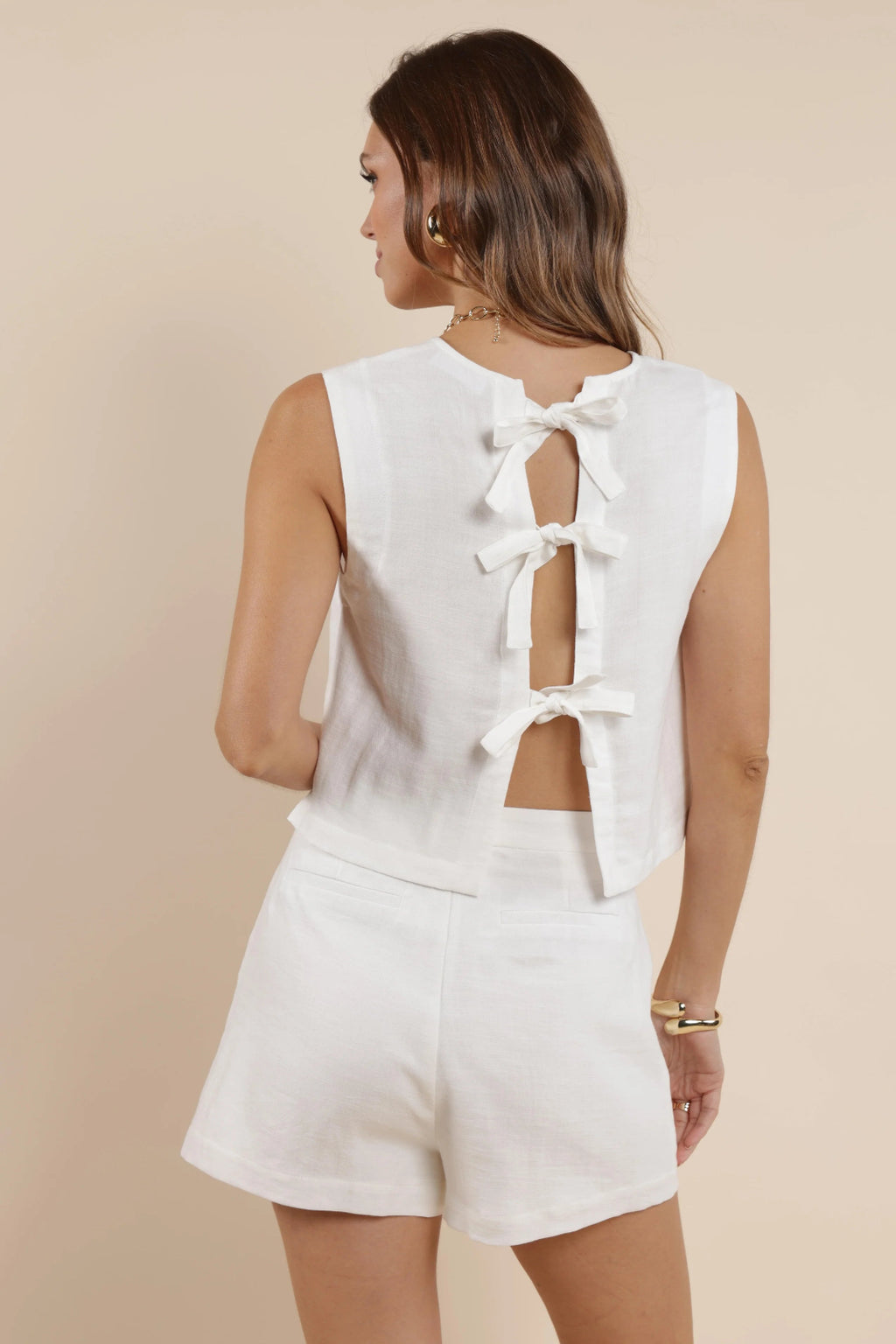 A back view of a girl wearing a white tank top with back bow ties and matching shorts.
