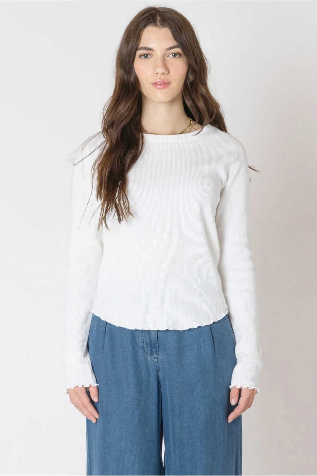 Woman wearing a white sweater and blue pants against a plain background.